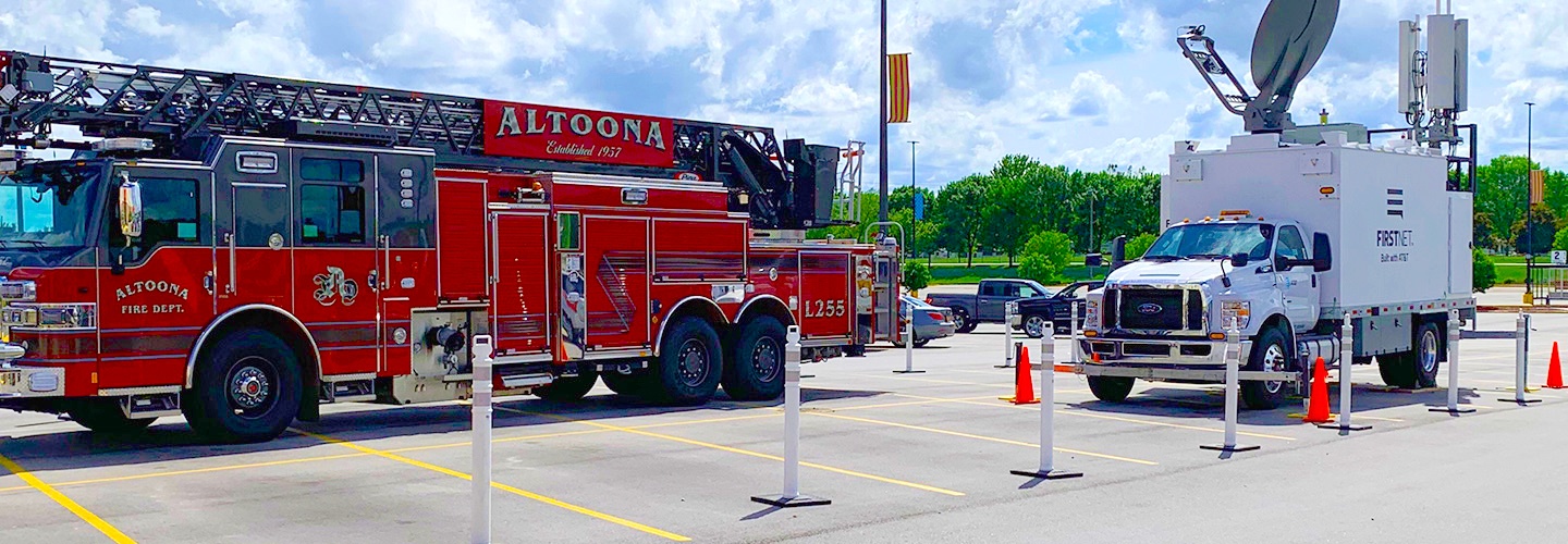 Two trucks in a parking lot on a cloudy day; a fire truck emblazoned with “Altoona Fire Department”; a FirstNet SatCOLT with “FirstNet Build With AT&T” on the side. 