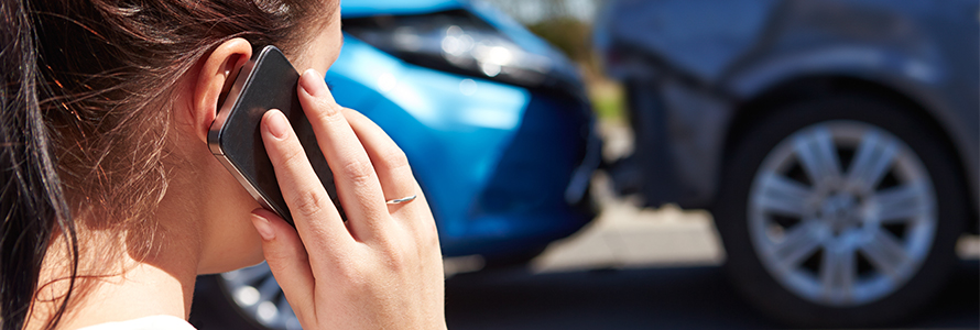 A woman making a phone call in front of a fender bender.