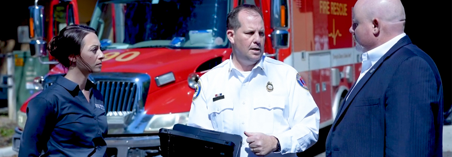 A FirstNet Authority staff member listens to a firefighter holding a mobile computer