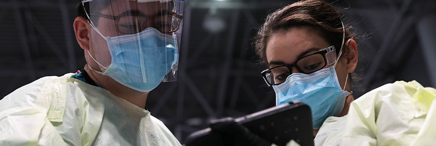 Two medical professionals waring masks look at a tablet