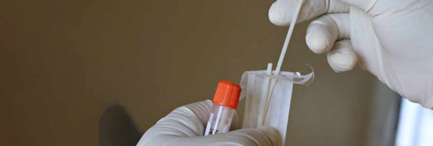 Gloved hands holding cotton swab being placed into a sample vial