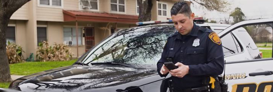 San Antonio Police officer near his car looking at a cell phone