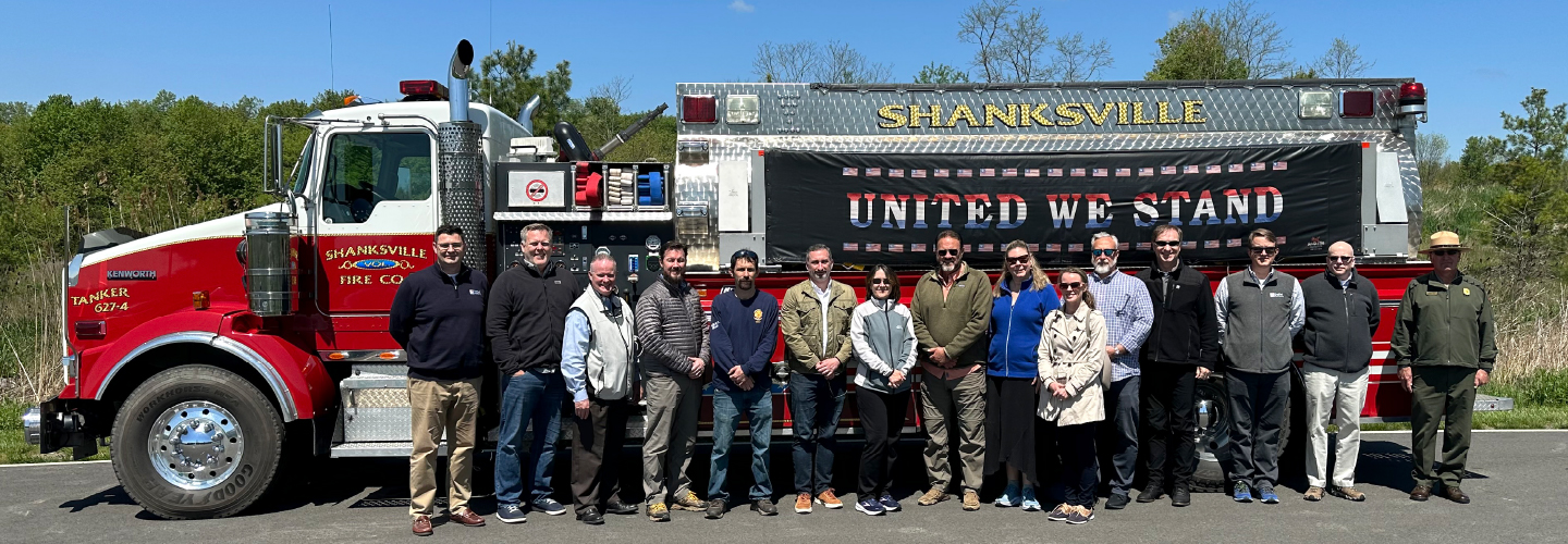 The First Responder Network Authority executive team stands in front of a Shanksville (Pa.) Fire Department fire truck with “United We Stand” banner