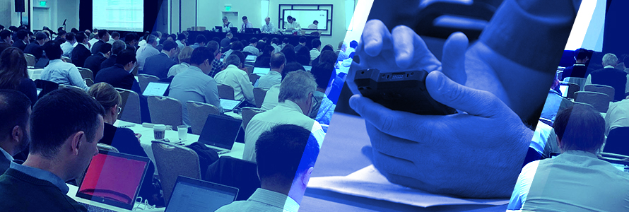 A room full of attendees at the June 2019 3GPP meetings listen and take notes on laptops as a panel of four speakers at the front give a presentation, a police officer holds a FirstNet enabled device