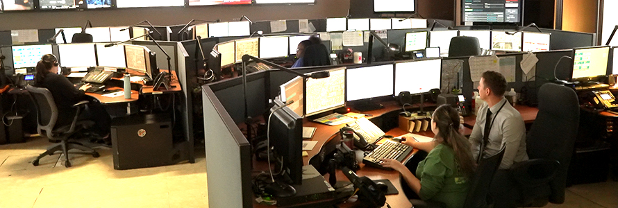 Miami-Dade dispatchers take calls and discuss issues inside of their center surrounded by information on various screens 