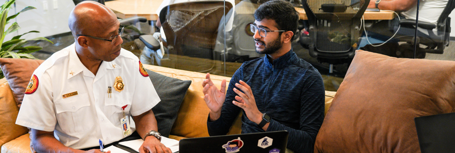 A firefighter sitting in an office with a programmer discussing public safety innovations