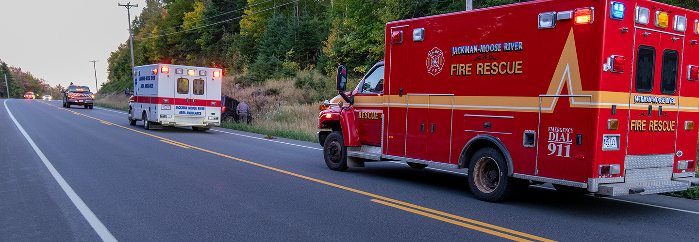 Ambulance and other vehicles from the Jackman Moose River Fire Rescue agency responding to a vehicle accident in a ditch beside a rural road. 