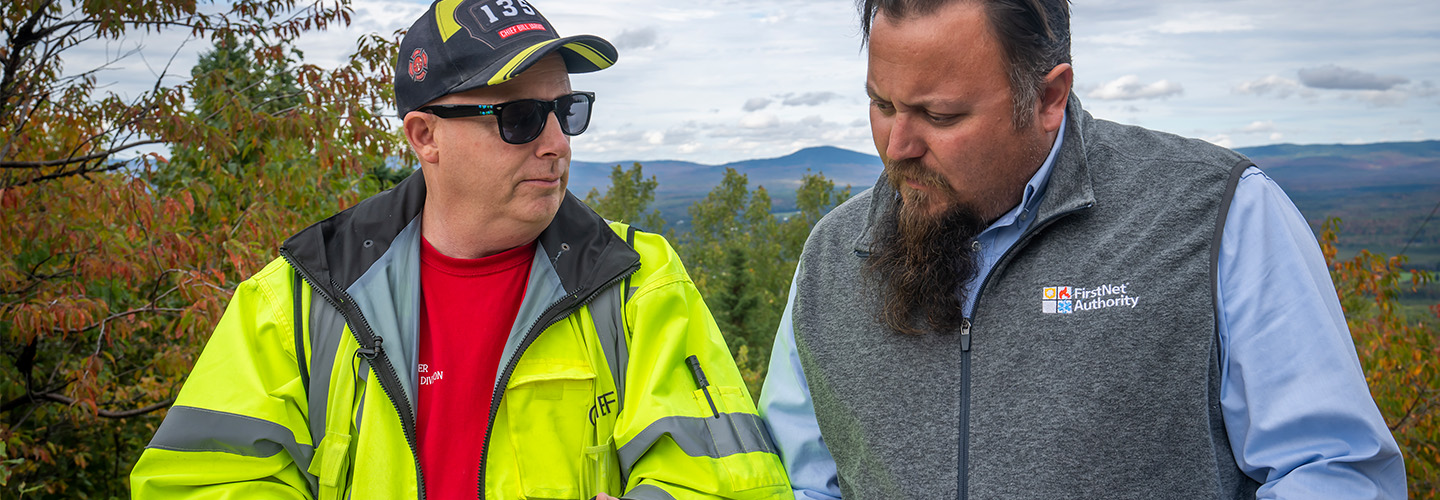 FirstNet Authority public safety advisor Bruce Fitzgerald talks with Jackman-Moose River Fire Chief Bill Jarvis with the mountains of Maine in the background during autumn