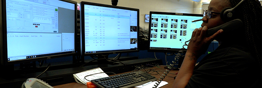 An emergency telecommunicator sits in front of computer monitor taking a call