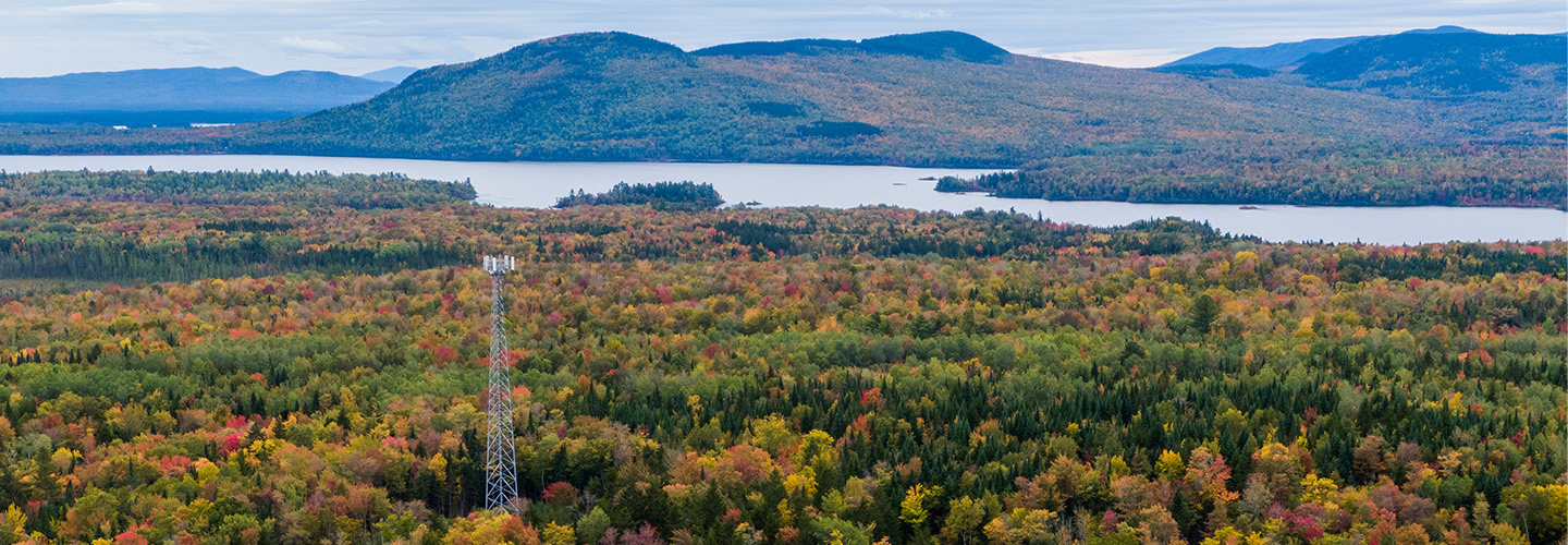 In rural Maine, a broadband cell tower rises over a landscape of forests, mountains, and lakes. 