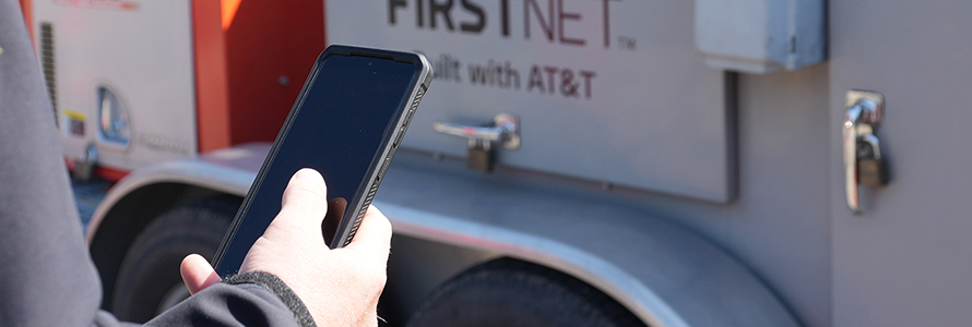 Police officer using a FirstNet enabled smartphone in front of a FirstNet SatCOLT