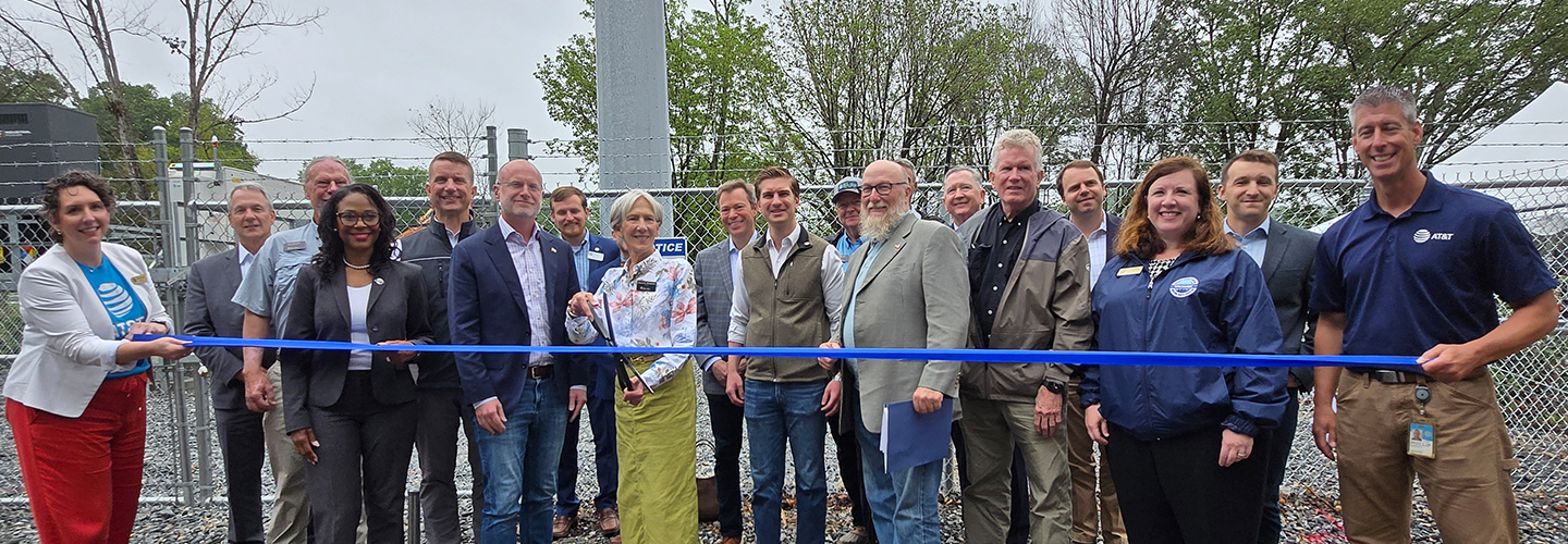 FirstNet Authority Executive Director and CEO Michael Cannon stands with federal, state and local leaders in front of a new cell tower with a blue ribbon in front. The mayor in the middle stands ready with scissors to cut the ribbon. 