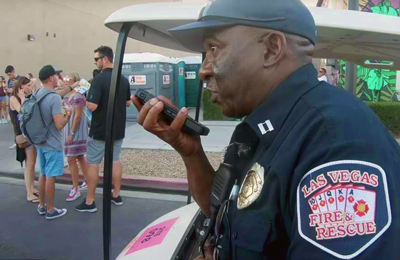 A City of Las Vegas Fire and Rescue uniformed officer speaks into a smartphone. Behind him are music festival attendees.