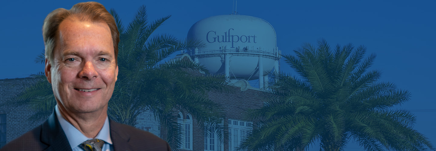 Mayor Billy Hewes’s headshot sits in front of a water tower with Gulfport written on it and foliage. 