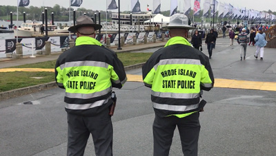 Two officers in Rhode Island State Police jackets look at the crowd at the 2018 Volvo Ocean Racenear the water