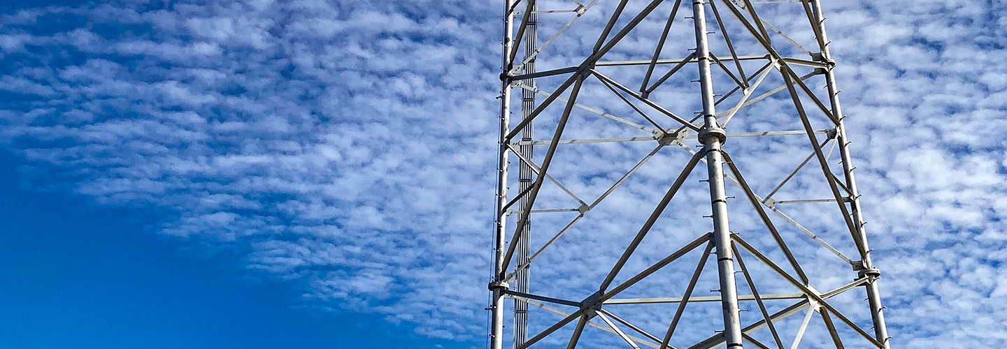 A broadband tower rises over a deep blue sky scattered with clouds