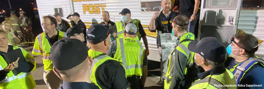 A group of first responders wearing yellow vests and medical masks gather outside an emergency response vehicle preparing to assist after a tornado near Jonesboro, Arkansas