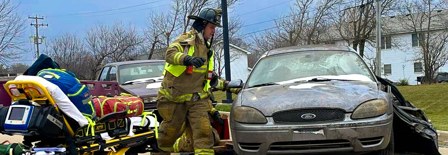 An EMS responder from the Bristol Kendall Fire Protection District with a stretcher at a damaged vehicle