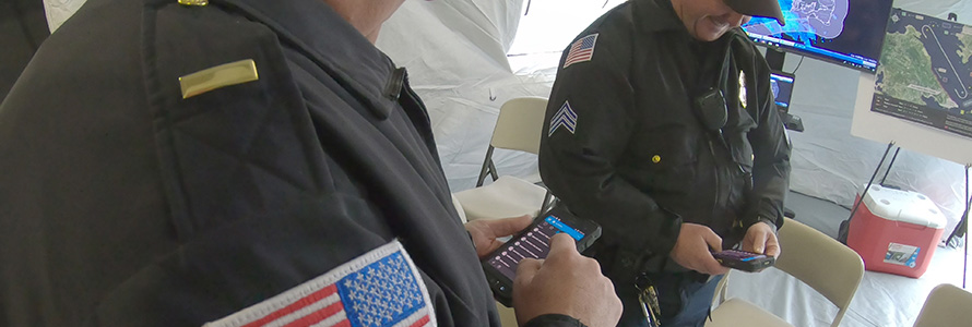 Two officers in uniform look down at FirstNet-enabled devices