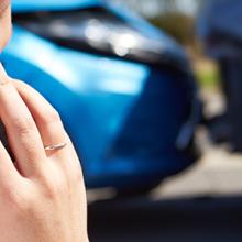 A woman making a phone call in front of a fender bender.
