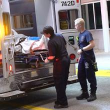 Two paramedics put a patient in the back of an ambulance.