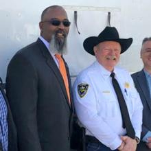 Sheriff Mike Hollinshead of Elmore County, Harry Markley from the FirstNet Authority and others stand in front of a FirstNet SatCOLT