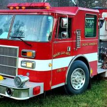 Shade Gap Area Fire Company fire vehicle stands in front of forested area and building, spraying water; Public Safety First podcast logo