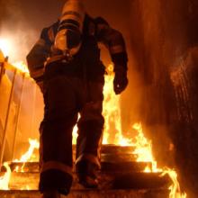 A firefighter ascends a flaming stairwell