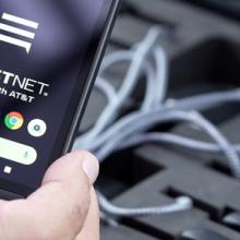 Hand holds a phone with the FirstNet logo over a case of additional cell phones.