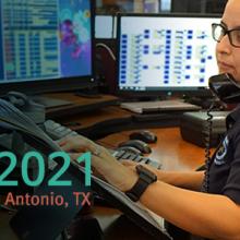 APCO 2021 logo; “APCO 2021; August 15-18|San Antonio, TX”; telecommunicator sits in front of monitors while taking a call.