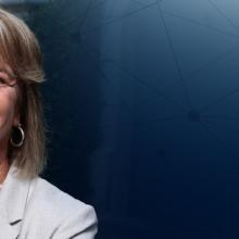 A headshot of FirstNet Authority Board Member Kristin Graziano, a backdrop of an office building and a series of network connections.