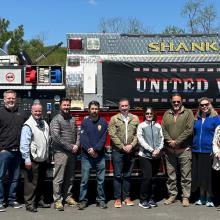 The First Responder Network Authority executive team stands in front of a Shanksville (Pa.) Fire Department fire truck with “United We Stand” banner