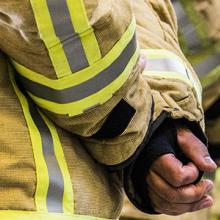 Firefighters stand in a line with their hands clasped behind their backs.