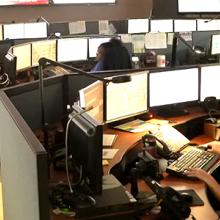 Miami-Dade dispatchers take calls and discuss issues inside of their center surrounded by information on various screens 