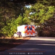 An ambulance drives down a small road on a sunny day. 