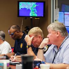 Pictured left to right sitting at a table with displays showing maps behind them: Gainesville (FL) Fire Chief Jeff Lane; Police Chief Tony Jones; Asst. Police Chief Terry Pierce; and Public Works Director Phil Mann.