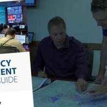 Four emergency managers gathered around table to survey multiple maps; front cover of the FirstNet Authority’s Emergency Resource Guide.