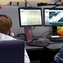 Two public safety officials look at multiple computer monitors at a workstation