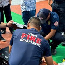 Members of the FirstNet Authority team and the Commonwealth of the Northern Mariana Islands Fire Department kneeling on the ground to demonstrate FirstNet assets during a multi-jurisdictional incident response communications exercise.