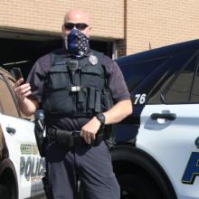 A police officer wearing a mask and a vest stands in front of a Green Bay Police vehicle A police officer wearing a mask and a vest stands in front of a Green Bay Police vehicle