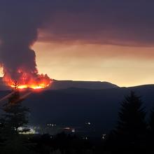 The Derby Fire burning on a distant mountain obscuring most of the sky with smoke while clouds in background are illuminated by the fire. 