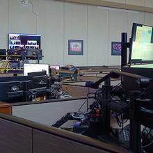 Three 9-1-1 call takers sit at dispatching consoles in a large 9-1-1 call center.