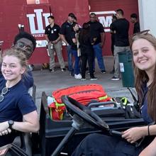 Four Intra-Collegiate Emergency Medical Service (IC-EMS) students smiling at the camera from electric carts while on duty at the Indiana University football stadium. 
