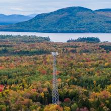 In rural Maine, a broadband cell tower rises over a landscape of forests, mountains, and lakes. 