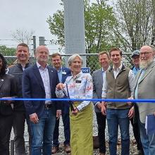 FirstNet Authority Executive Director and CEO Michael Cannon stands with federal, state and local leaders in front of a new cell tower with a blue ribbon in front. The mayor in the middle stands ready with scissors to cut the ribbon. 
