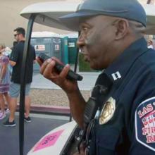 A City of Las Vegas Fire and Rescue uniformed officer speaks into a smartphone. Behind him are music festival attendees.