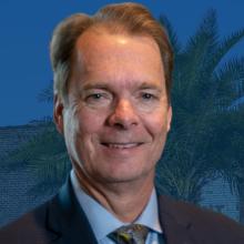 Board member Mayor Billy Hewes prioritize real-time communication for public safety Mayor Billy Hewes’s headshot sits in front of a water tower with Gulfport written on it and foliage.