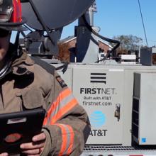 Firefighter using smart device in front of FirstNet deployable tower