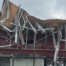 A person looks up at commercial building with the roof and storefront caved in from a tornado in Otsego County