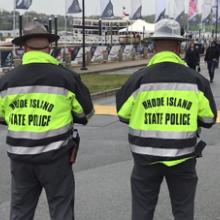 Two officers in Rhode Island State Police jackets look at the crowd at the 2018 Volvo Ocean Racenear the water